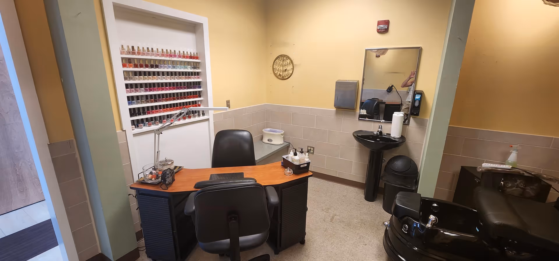 Nail salon inside a senior care facility with nail polish rack, desk, mirror, and pedicure chair.
