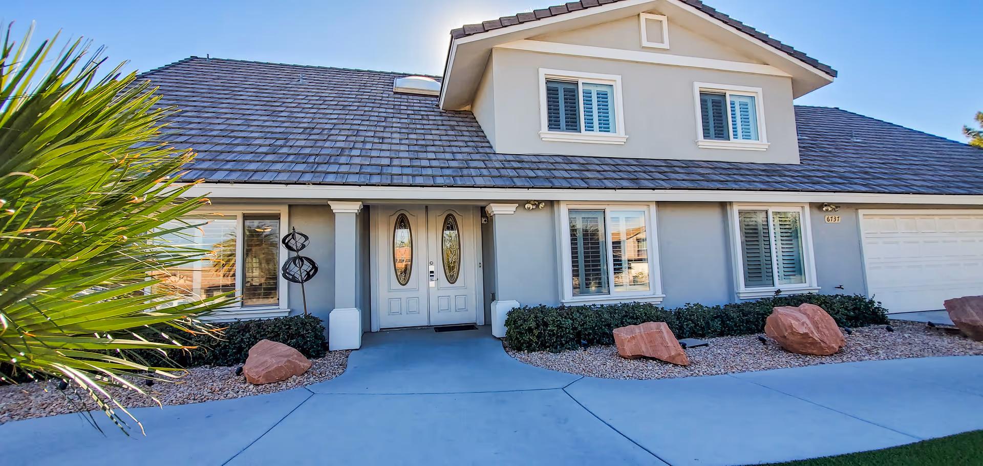 Front view of a suburban house with double entry doors, garage, and rock landscaping.