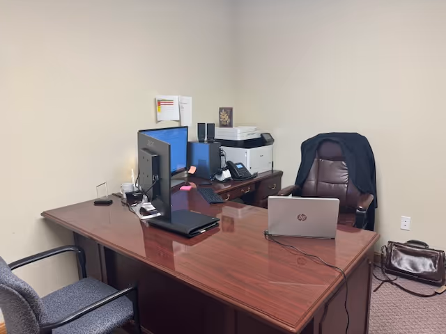 Office desk with dual monitors, laptop, and printer in a care facility.