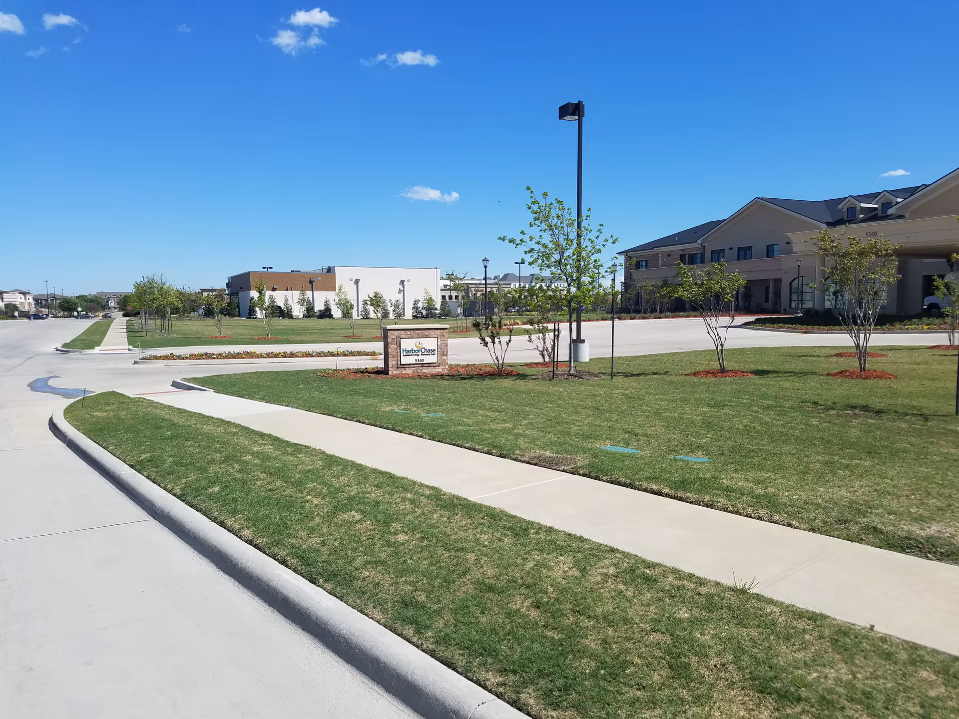 Wide view of HarborChase of Plano exterior with manicured lawn and street.