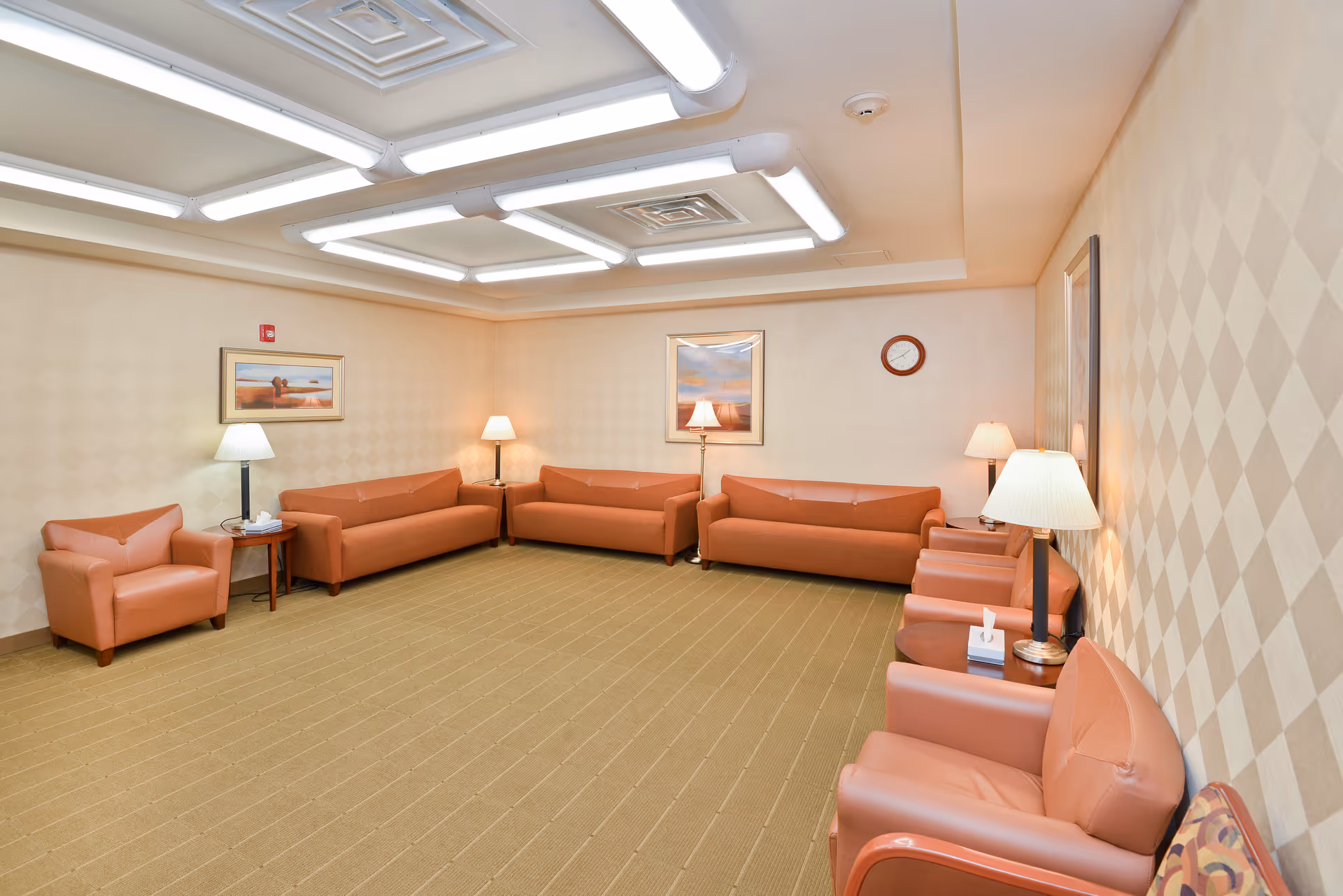A spacious beige lounge with orange leather sofas, lamps, and framed art.
