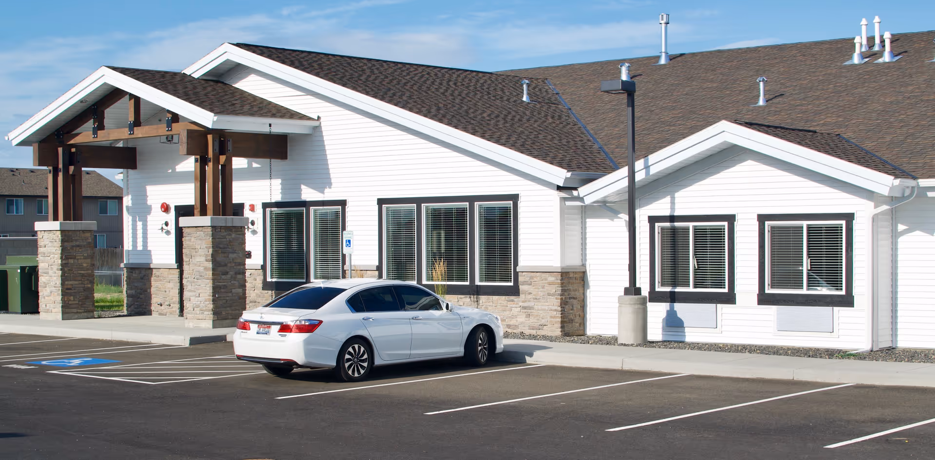 Front exterior of a single-story white building with stone accents and a white car parked in the lot.