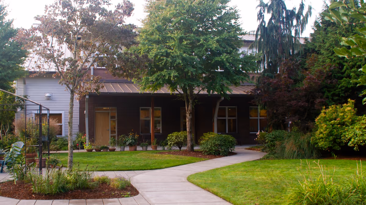 Front exterior of a senior living facility with a curved walkway and landscaped greenery.