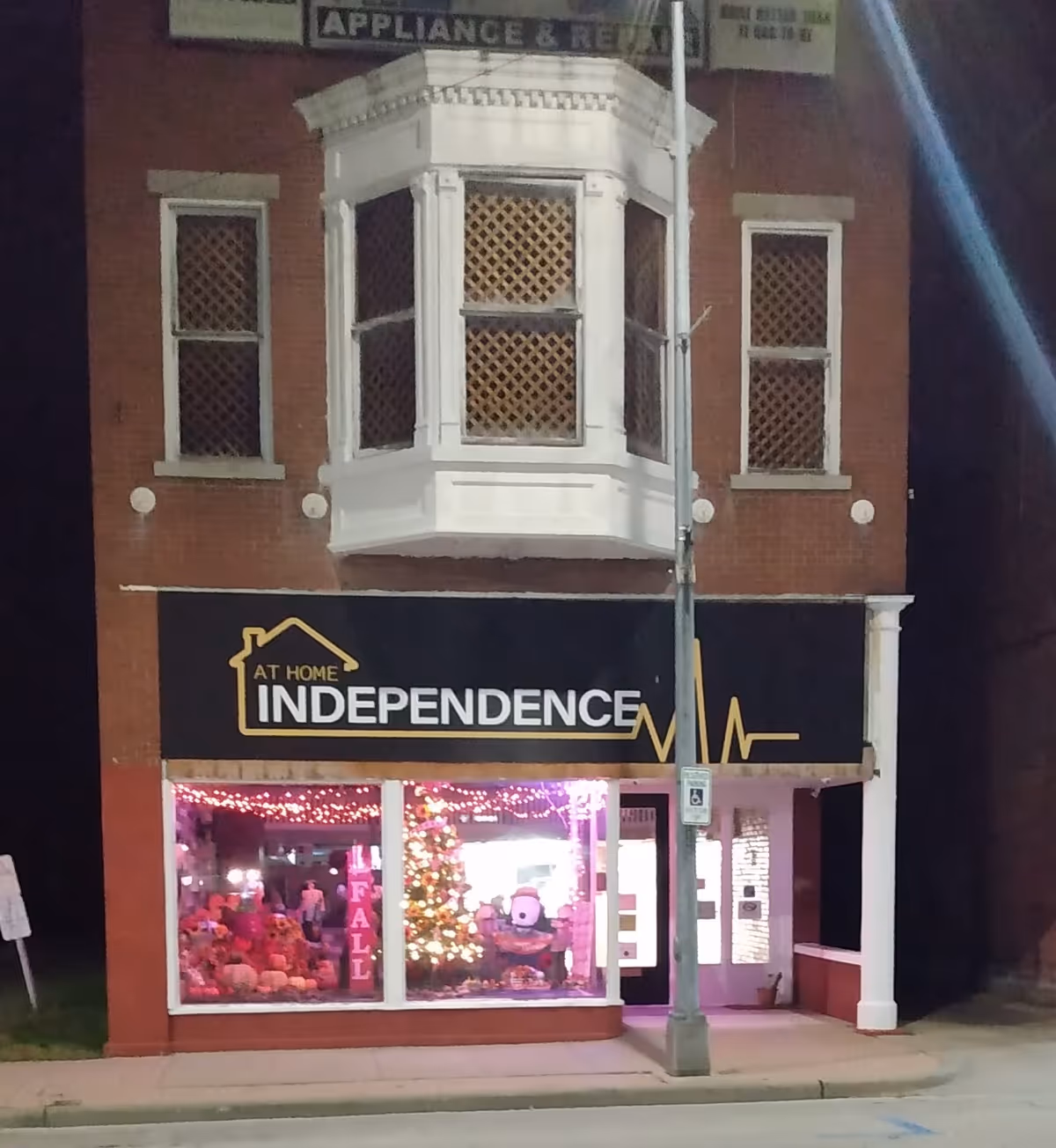 A brick two-story building with a black storefront sign reading At Home Independence and holiday display