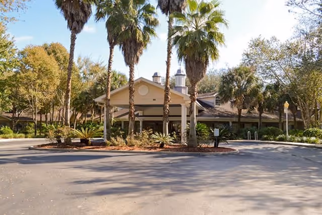 Front view of Charter Senior Living of Gainesville with palm trees and a circular driveway.