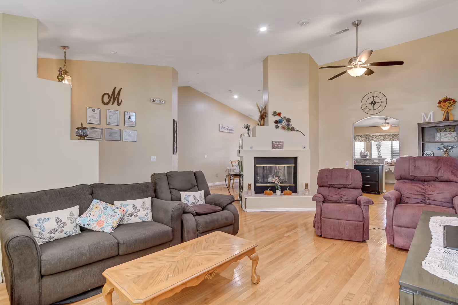 Cozy senior living lounge with couches, recliners, fireplace, and warm wood flooring.