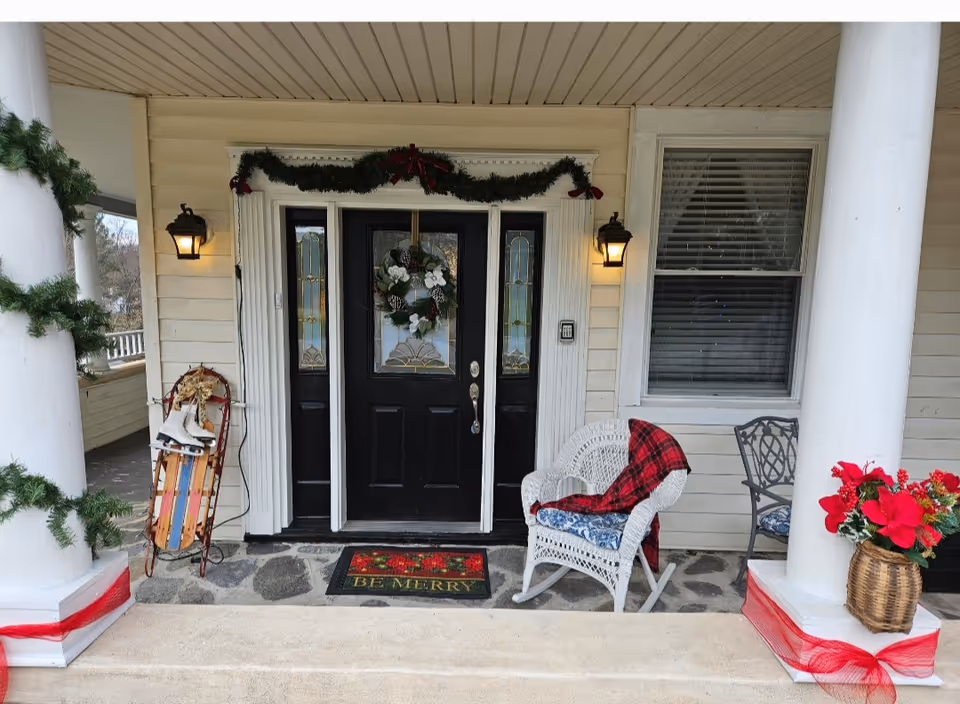 Decorated front porch of Hampton Meadows Assisted Living with wreath, garland, chairs, and welcome mat