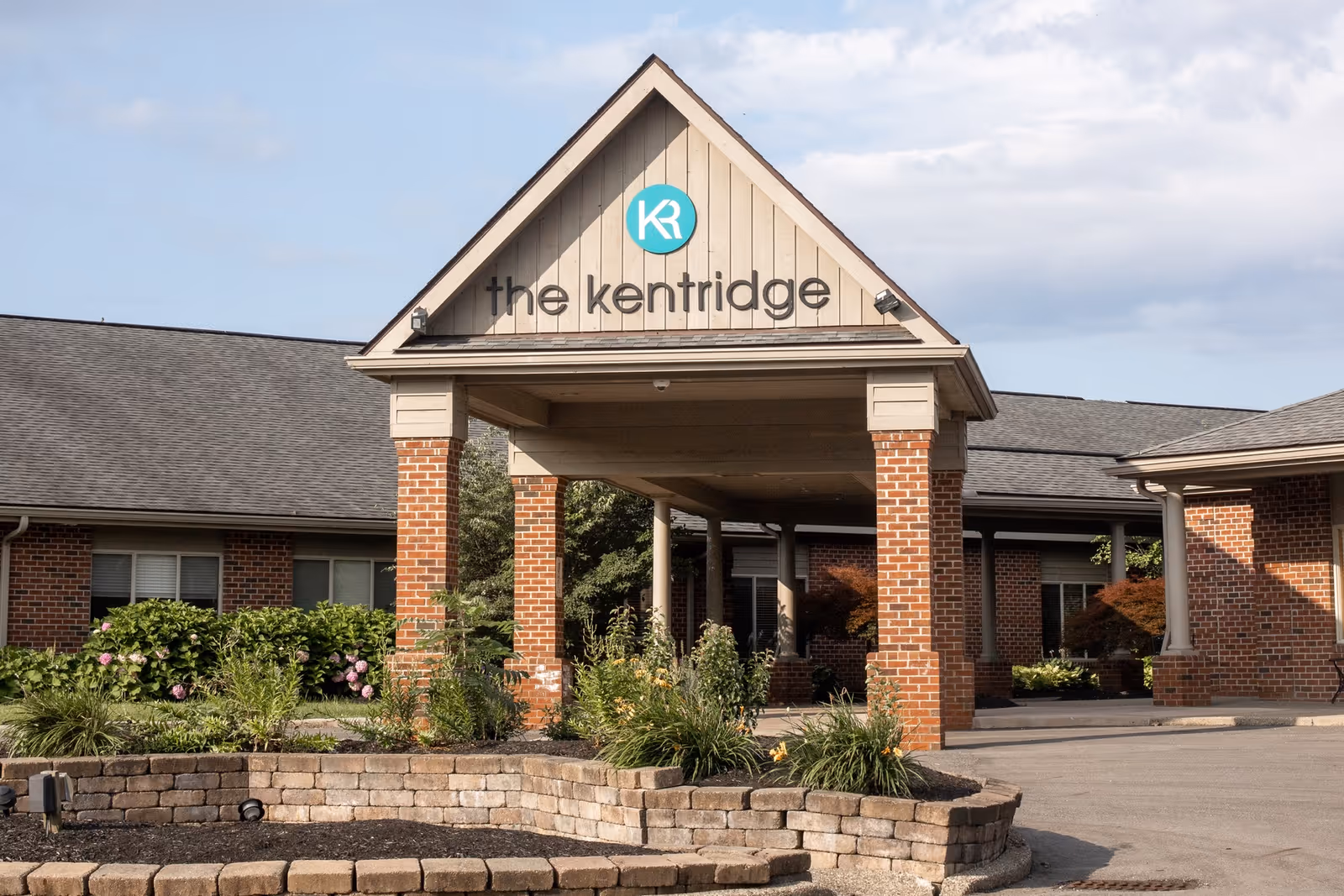 Brick-built main entrance with a covered drop-off and landscaped garden at The KentRidge Senior Living.