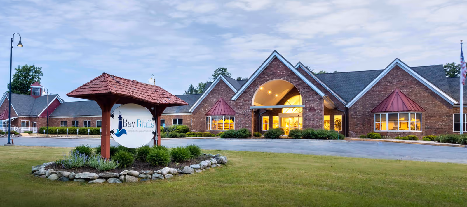 Brick senior living building with illuminated front entrance and landscaped sign.