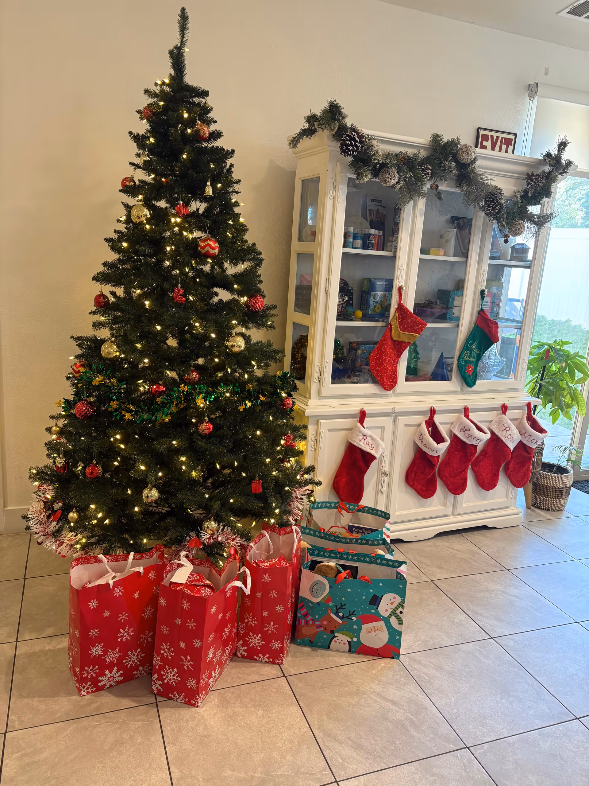 Christmas tree, stockings, garland, and gift bags decorate a bright facility lobby.