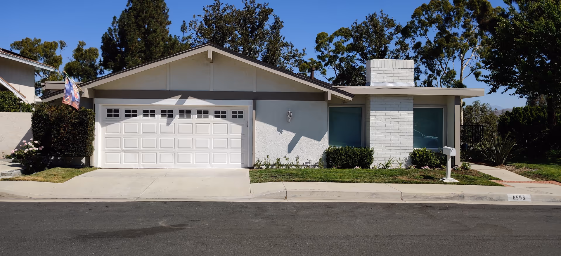 Front view of a single-story white-and-gray house with a two-car garage and an American flag
