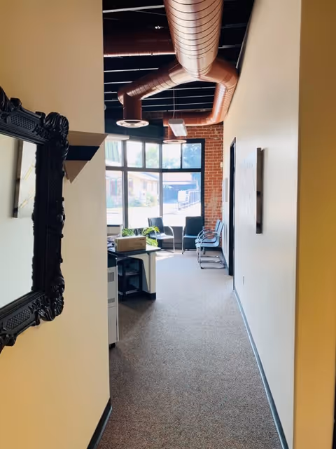 Hallway leads to a bright lounge area with seating by large windows.