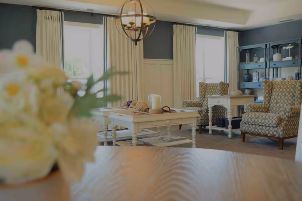 Senior living room with patterned chairs, white coffee tables, shelving, and a pendant light.