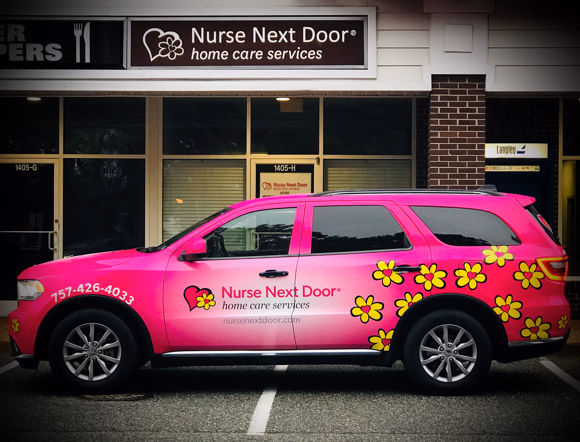 Bright pink Nurse Next Door van with yellow flowers parked in front of a care office.