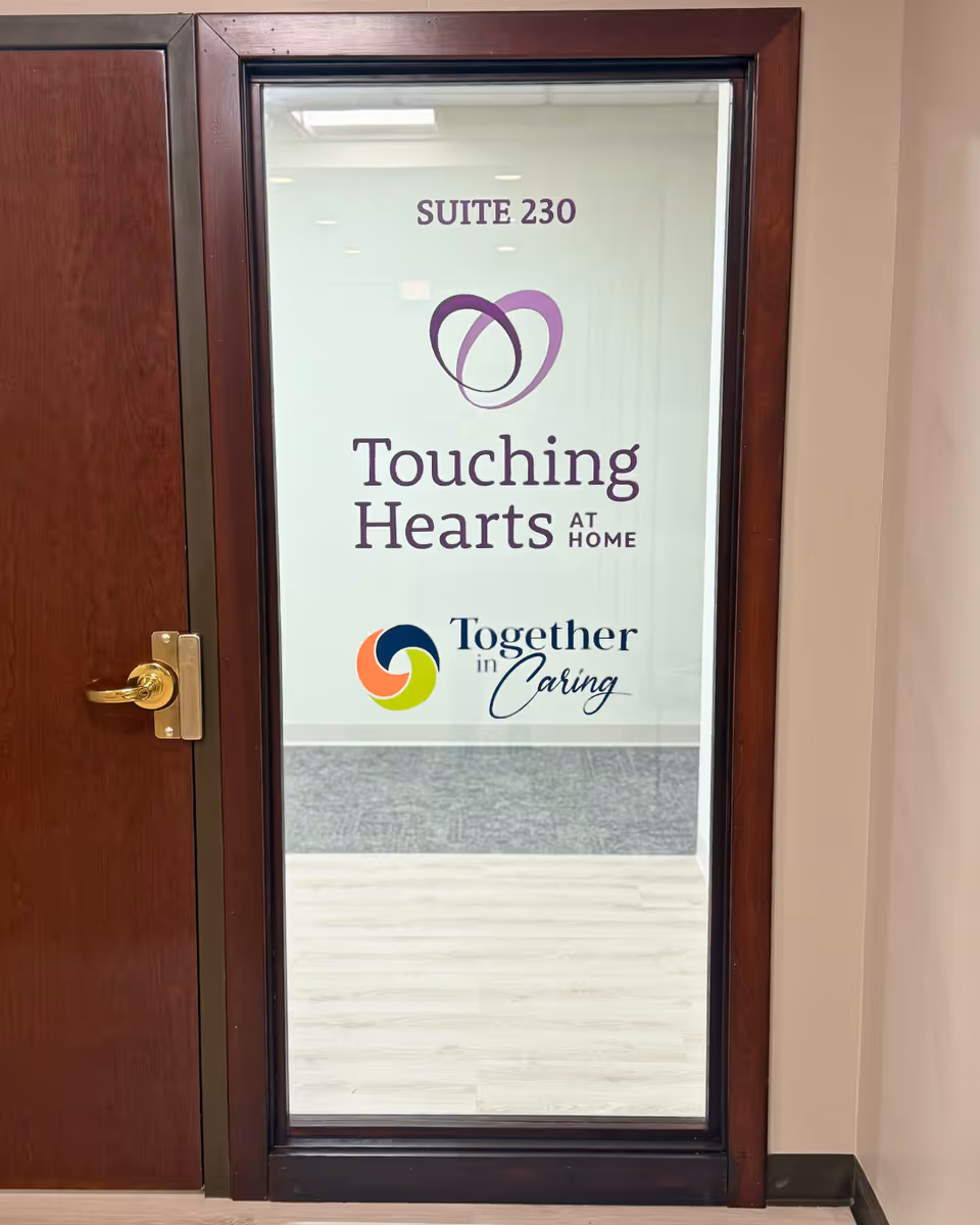 Glass interior door displaying Suite 230 sign and Touching Hearts at Home, Together in Caring logos.