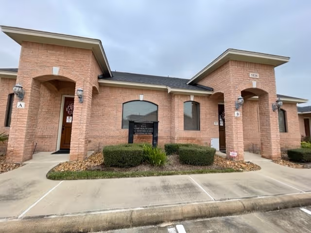 Brick senior-living facility building with two arched entrances and a small landscaped front garden.