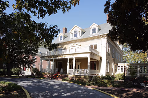 Front exterior view of a two-story assisted living facility with a porch and landscaping