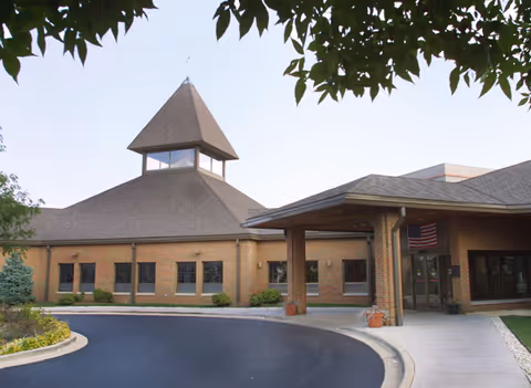 Brick senior living facility with covered entrance and circular driveway; trees frame the top.