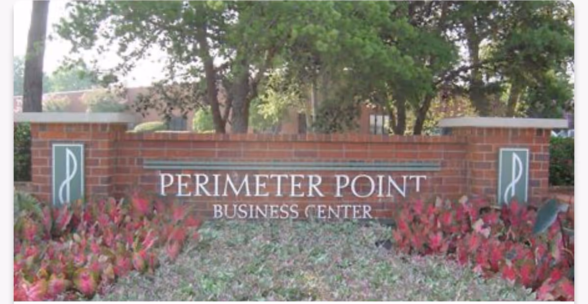 Brick entrance sign reading PERIMETER POINT BUSINESS CENTER with surrounding plants and trees.