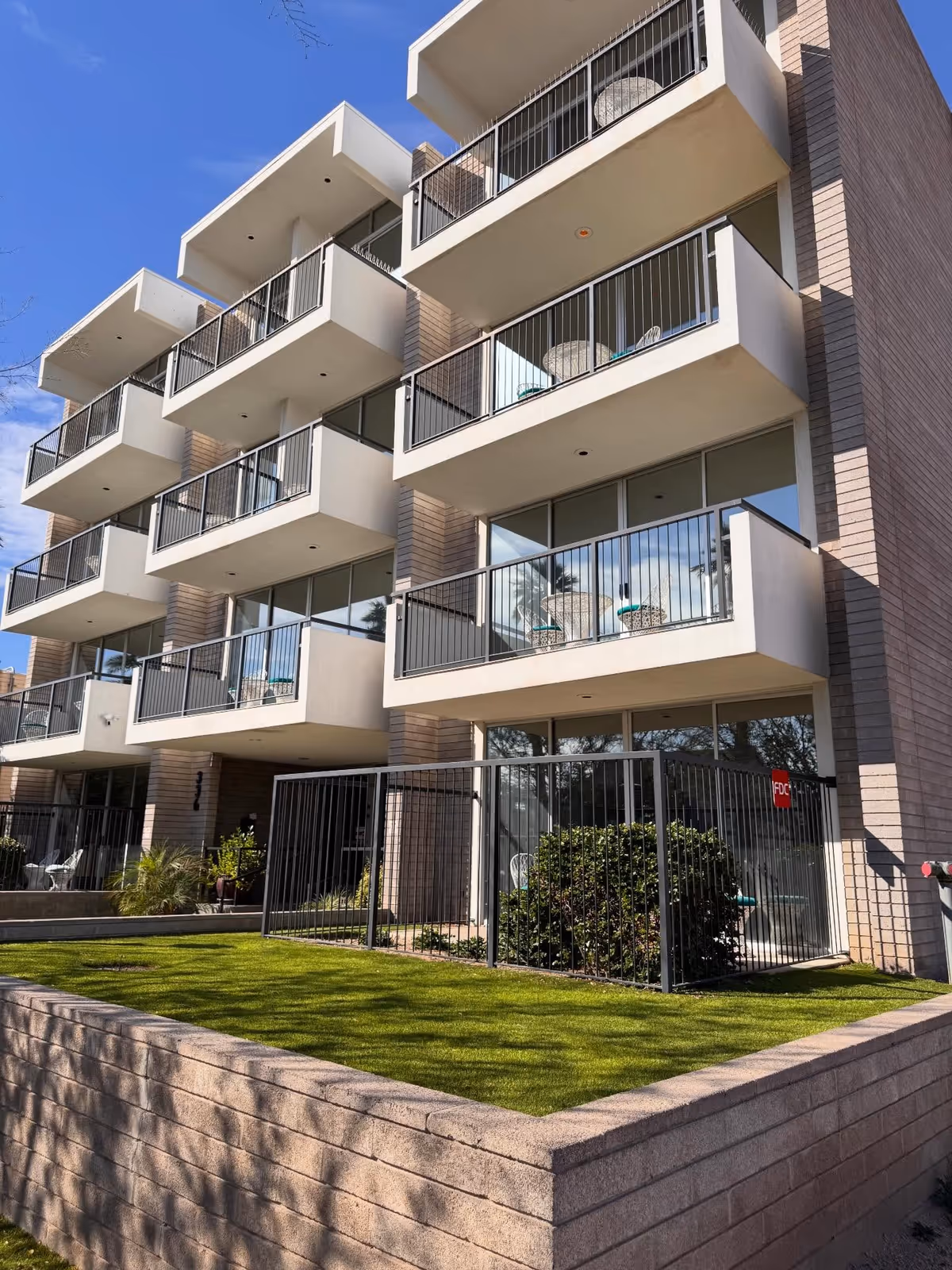 Modern multi-story senior housing exterior with balconies, glass doors, and a grassy courtyard.