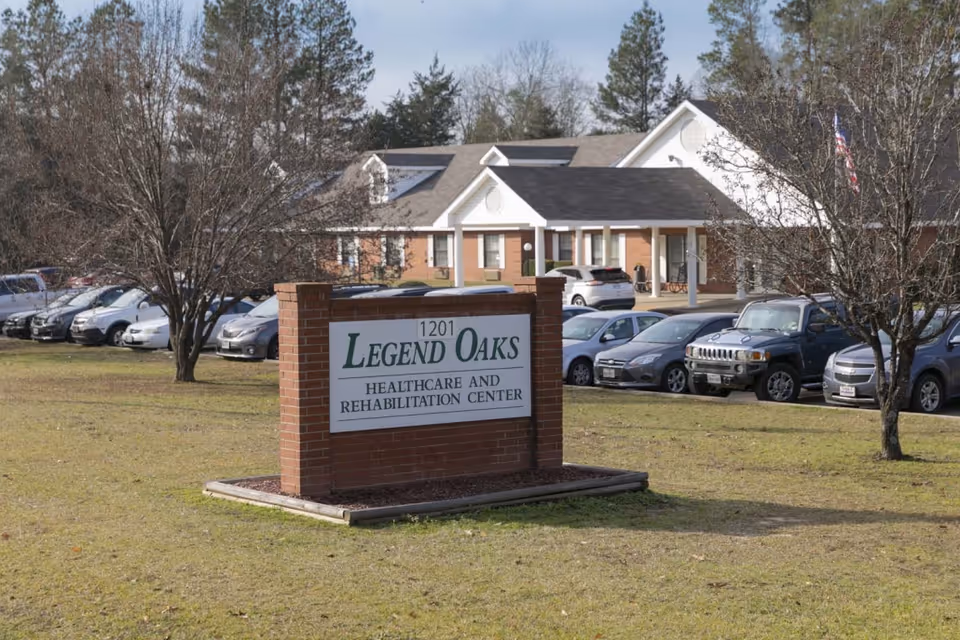 Exterior view of Legend Oaks facility with brick sign and parked cars.