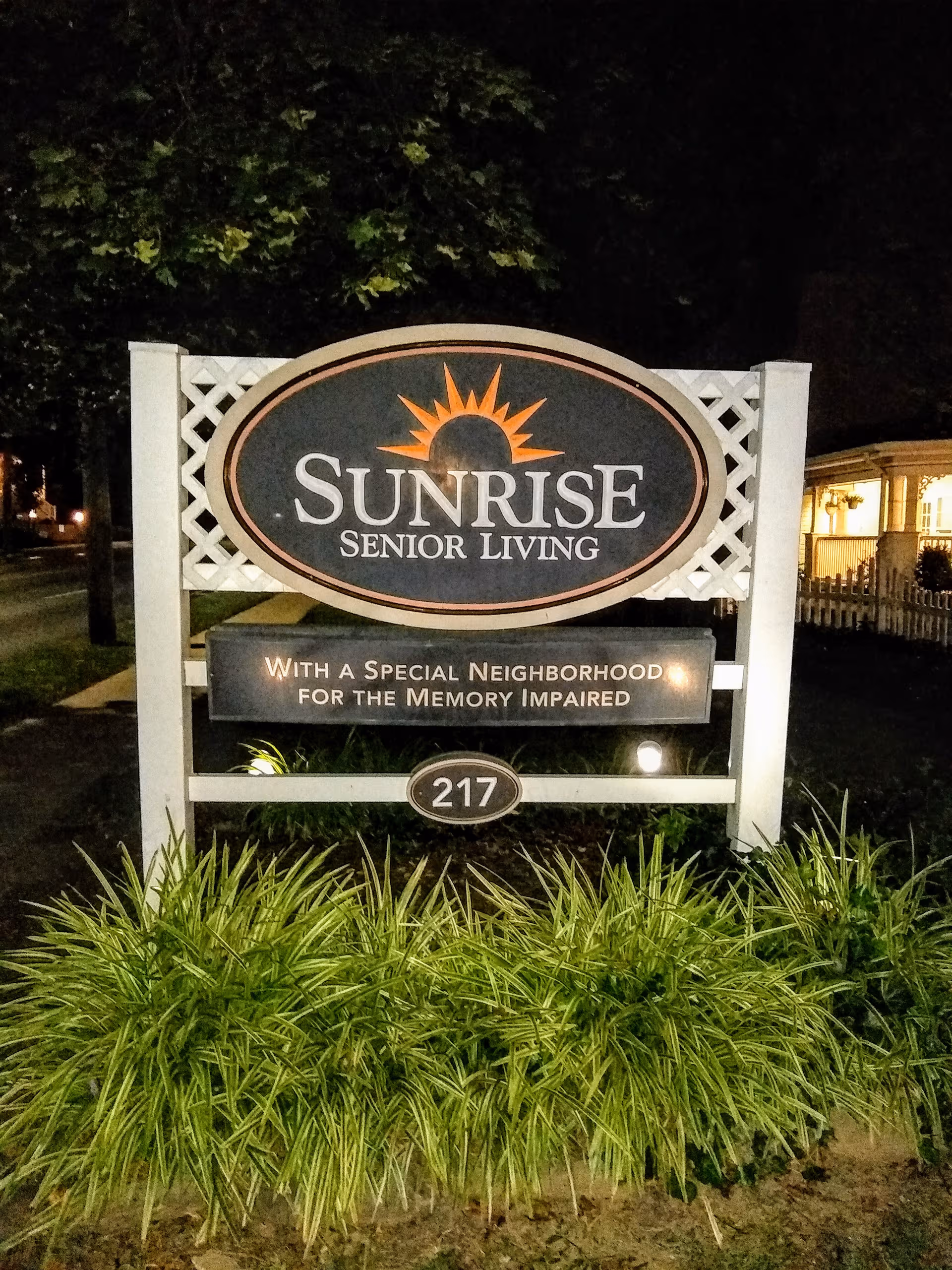 Sunrise Senior Living sign with landscaping at night.