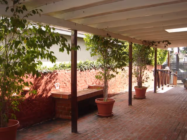 Covered outdoor walkway with brick flooring, potted trees, and a brick bench along the wall.