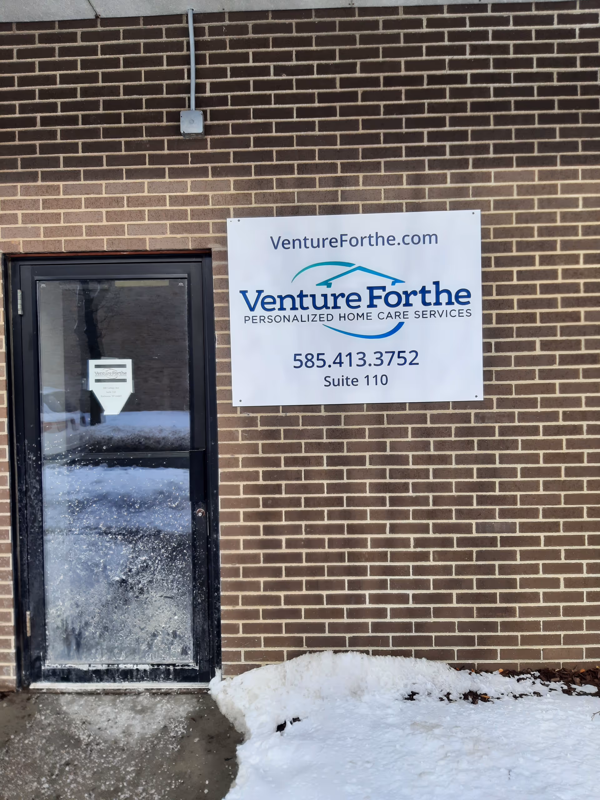 Brick building exterior with a VentureForthe sign, glass door, and snow on the ground.