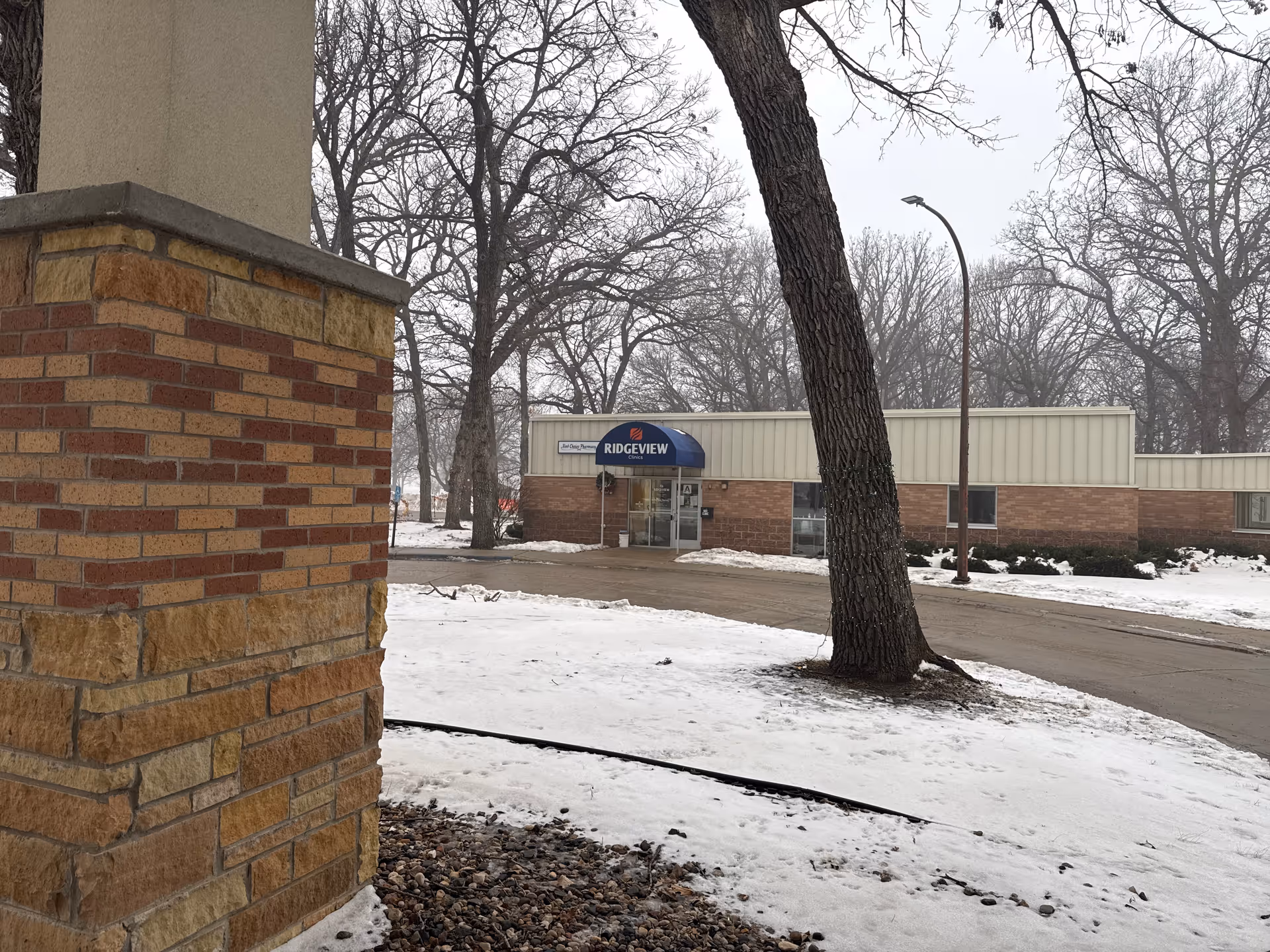 Snowy exterior of a brick-front senior living building with a blue awning at the entrance.