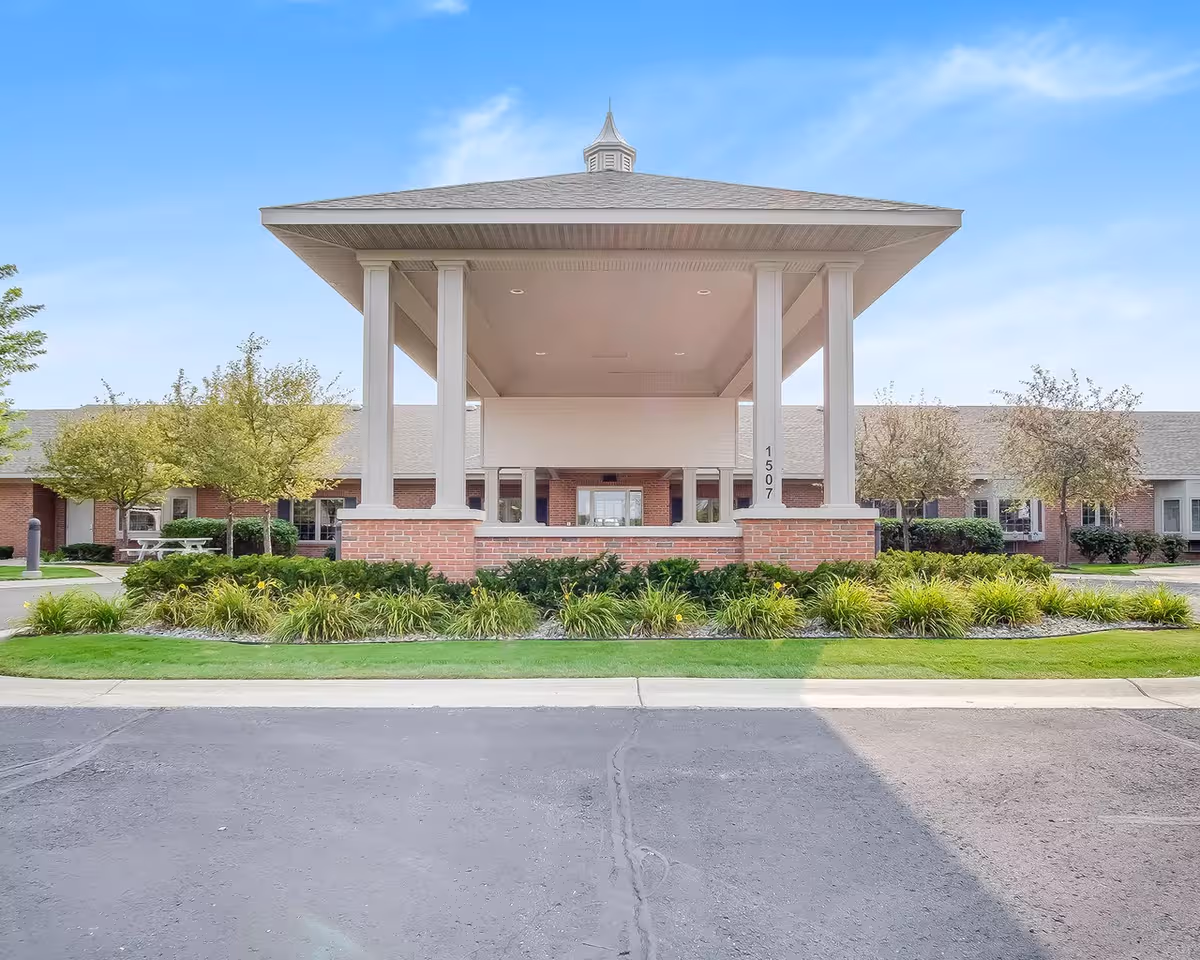 A modern assisted living facility entrance with a large shaded portico and landscaped front