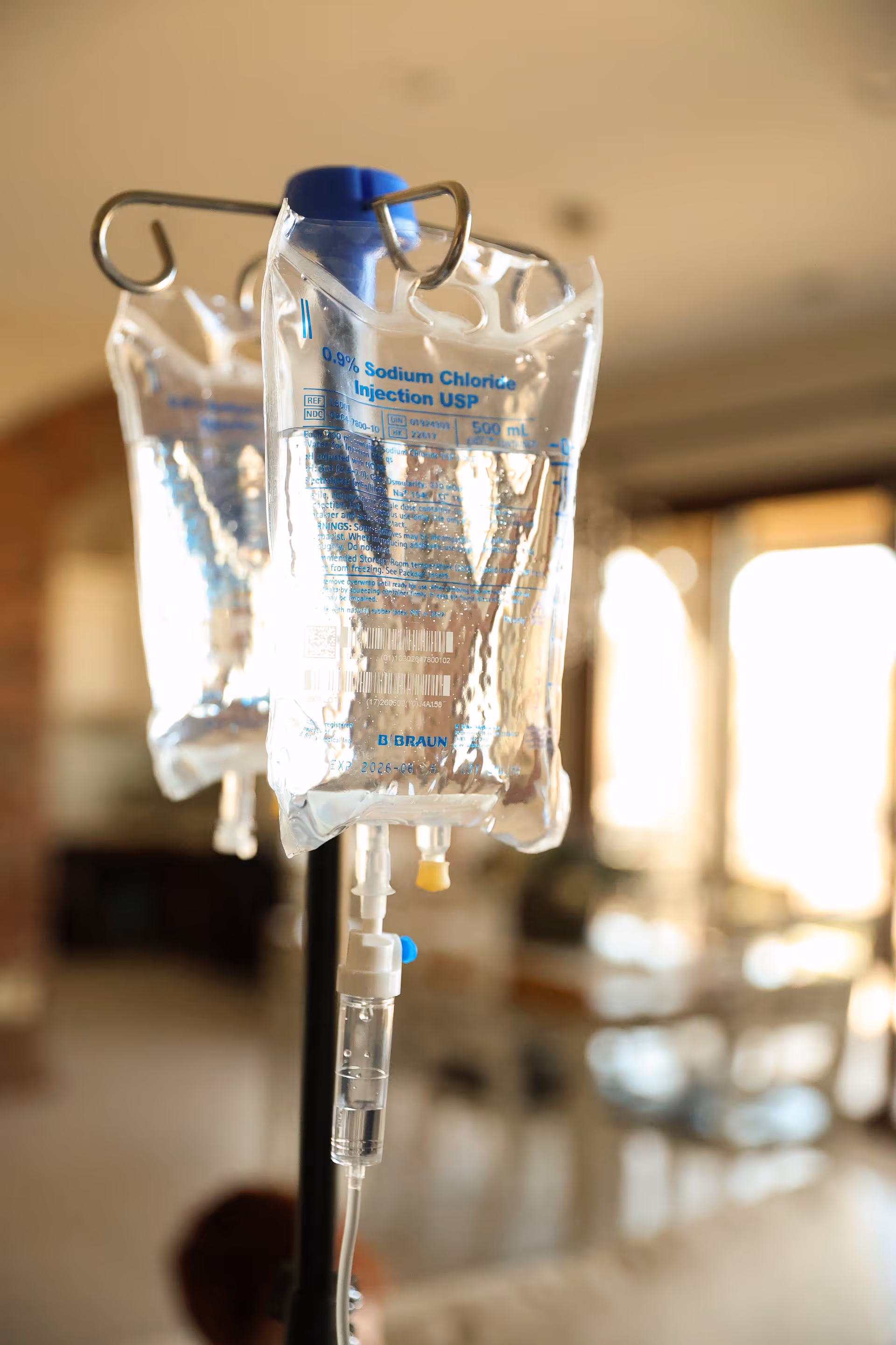 IV infusion bags hang from stands in a bright, clinical senior living facility interior.