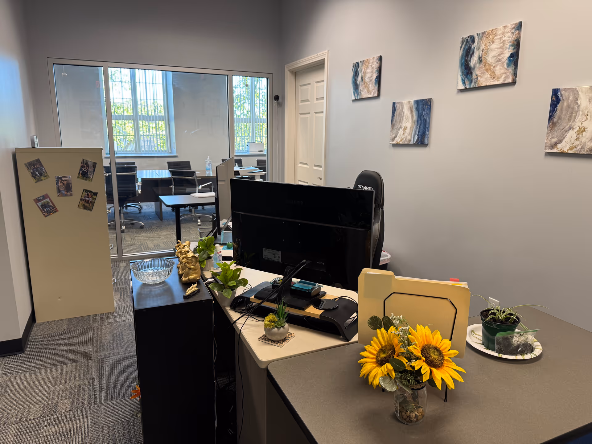 Reception desk with computer and sunflower arrangement in an office overlooking a glass-walled meeting room