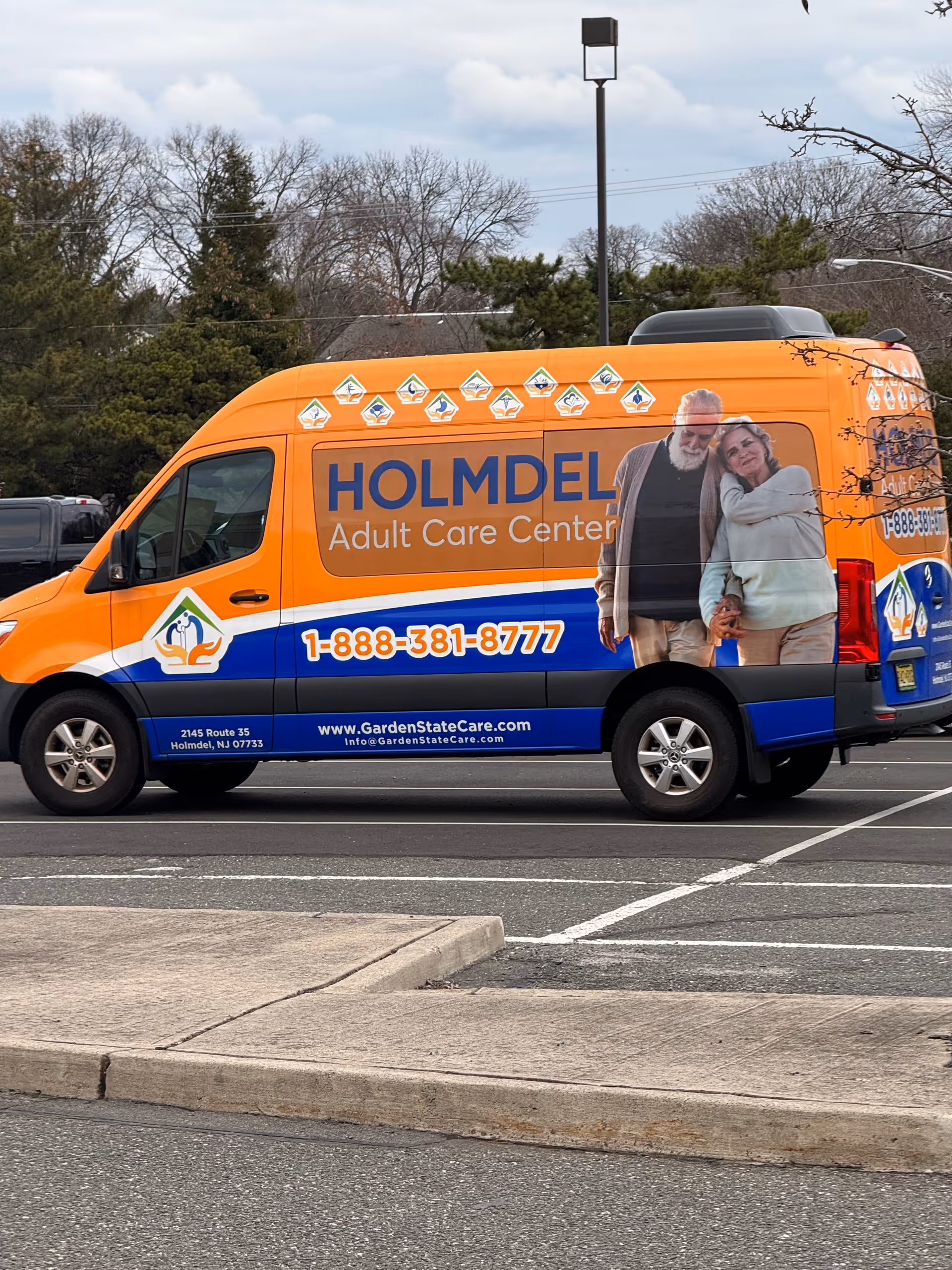 An orange Holmdel Adult Care Center van with a couple image parked in a lot.
