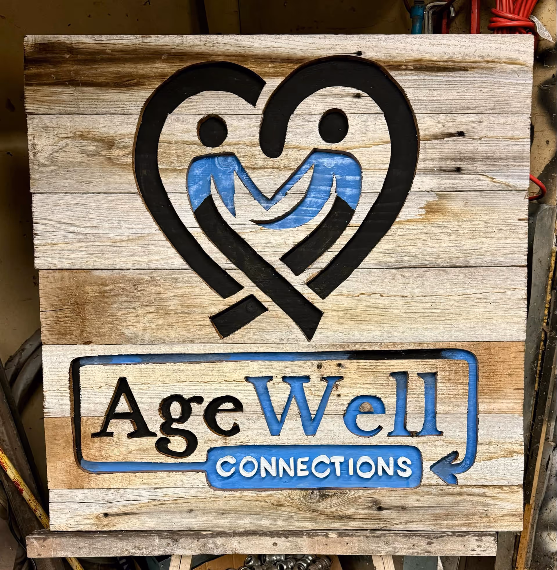 Wooden signboard with AgeWell Connections logo and name outdoors on weathered planks.