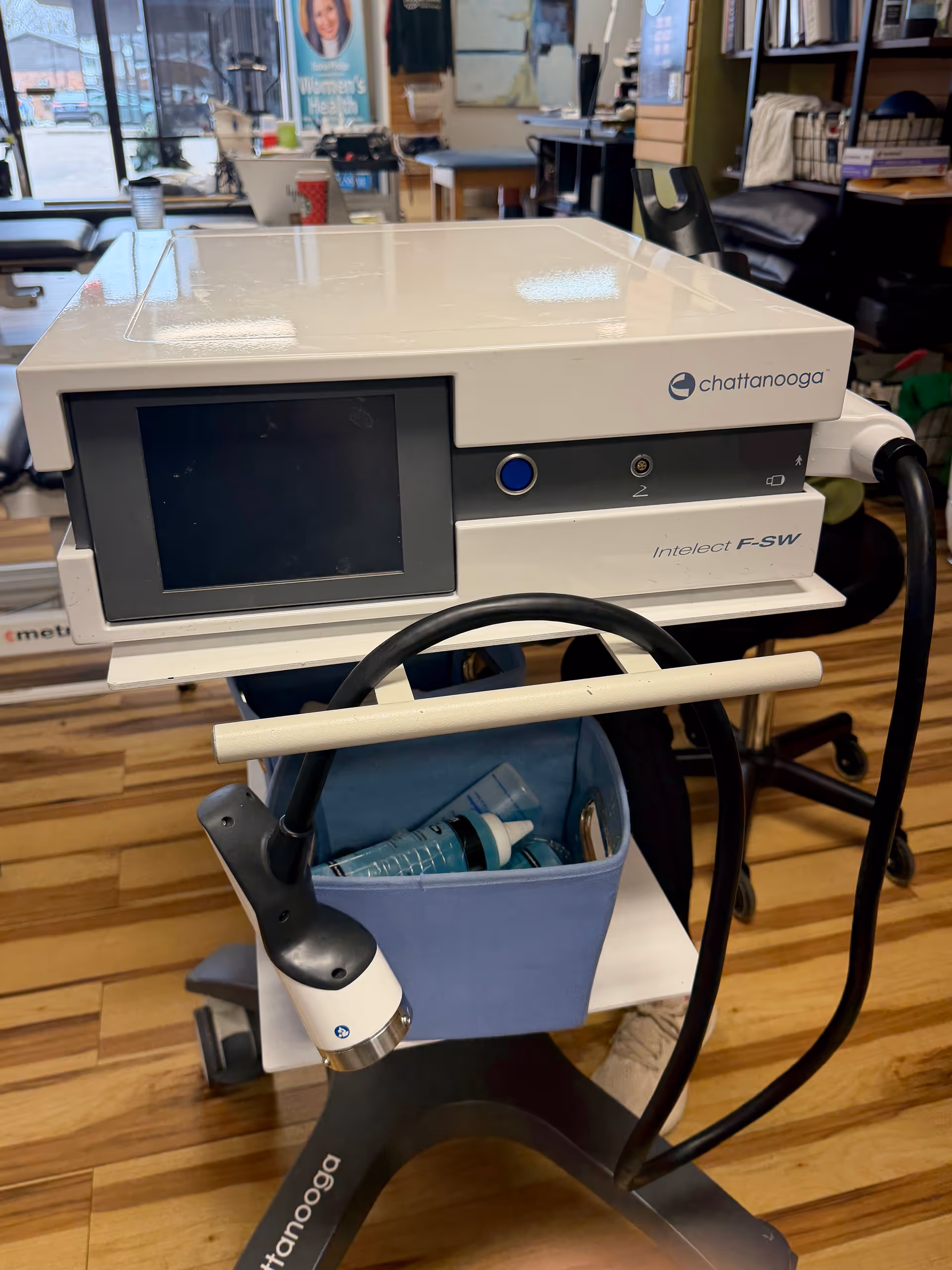 Medical therapy device on a wheeled cart in a clinic room with supplies.