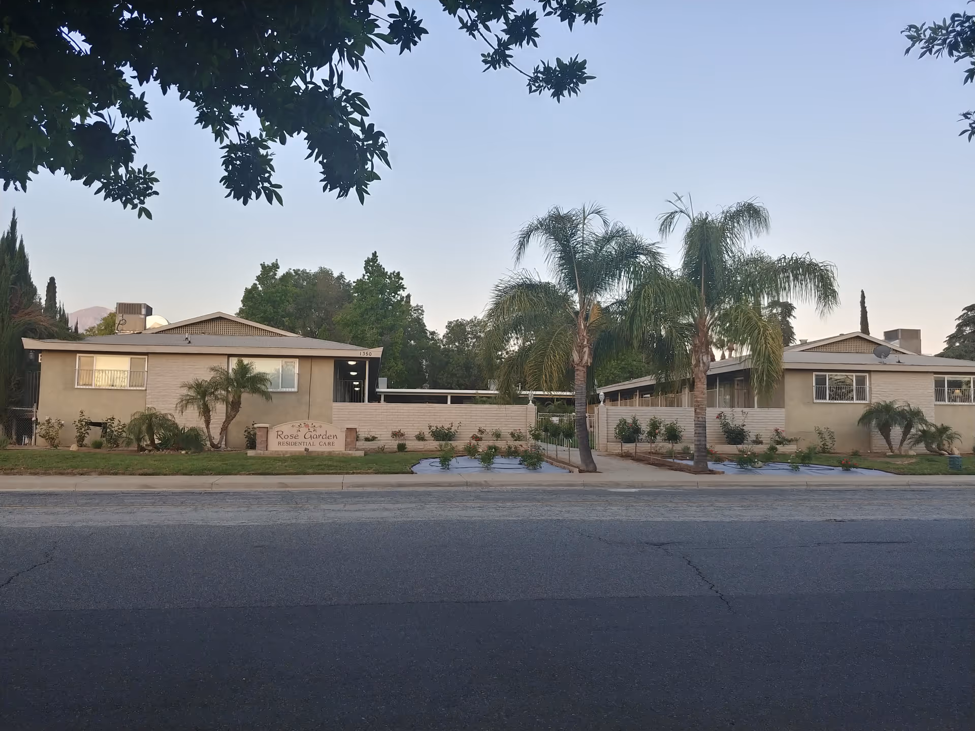 Wide exterior view of Rose Garden Residential Care building with palm trees.