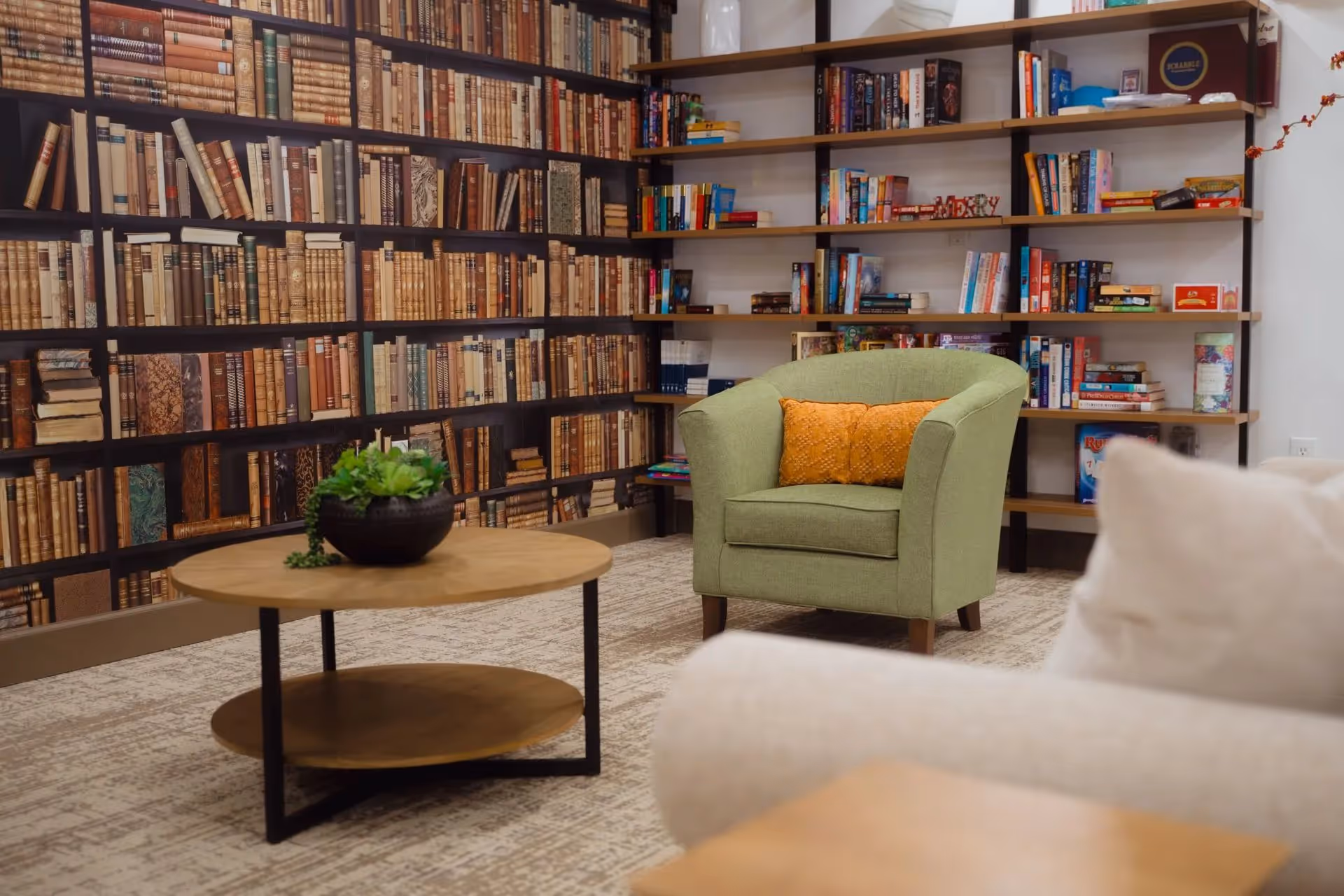 A cozy library lounge with shelves full of books, a green armchair, and a coffee table.
