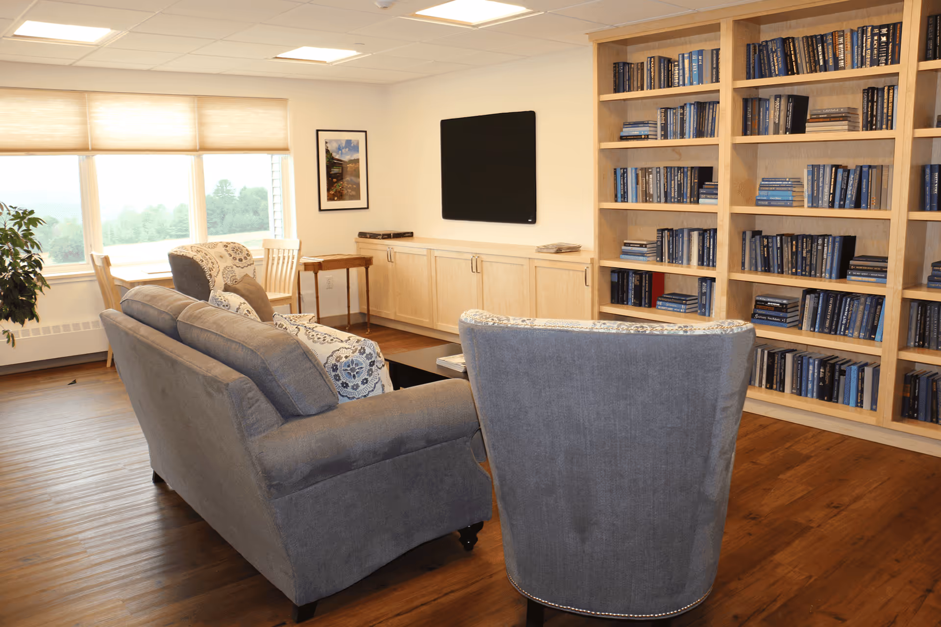 Cozy living room with blue sofas, a wall-mounted TV, and tall bookshelf cabinets.