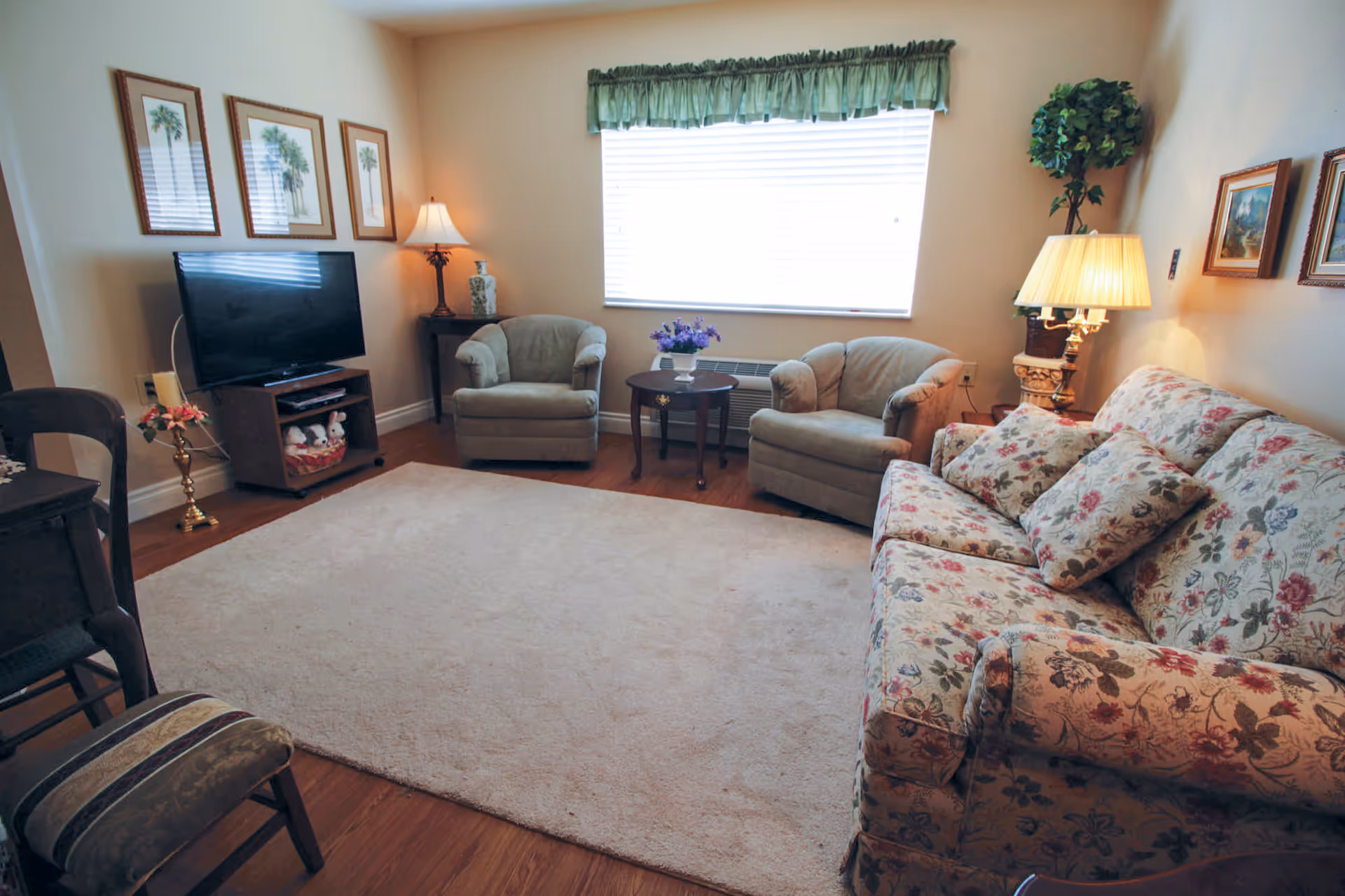 Cozy living room with floral sofa, two armchairs, TV, and warm lamps.