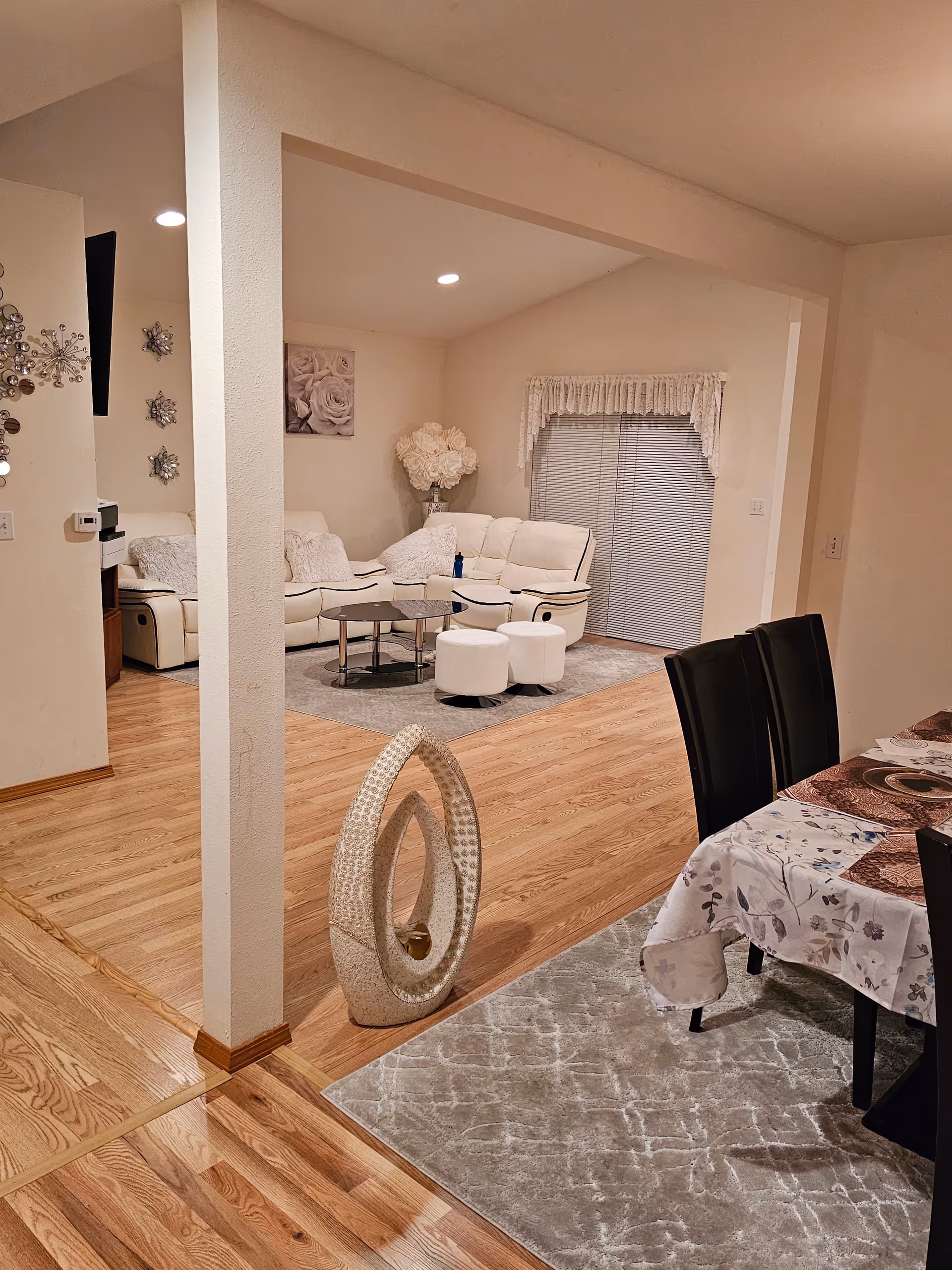 Bright living room with white leather seating, round glass coffee table, rug, and dining area.