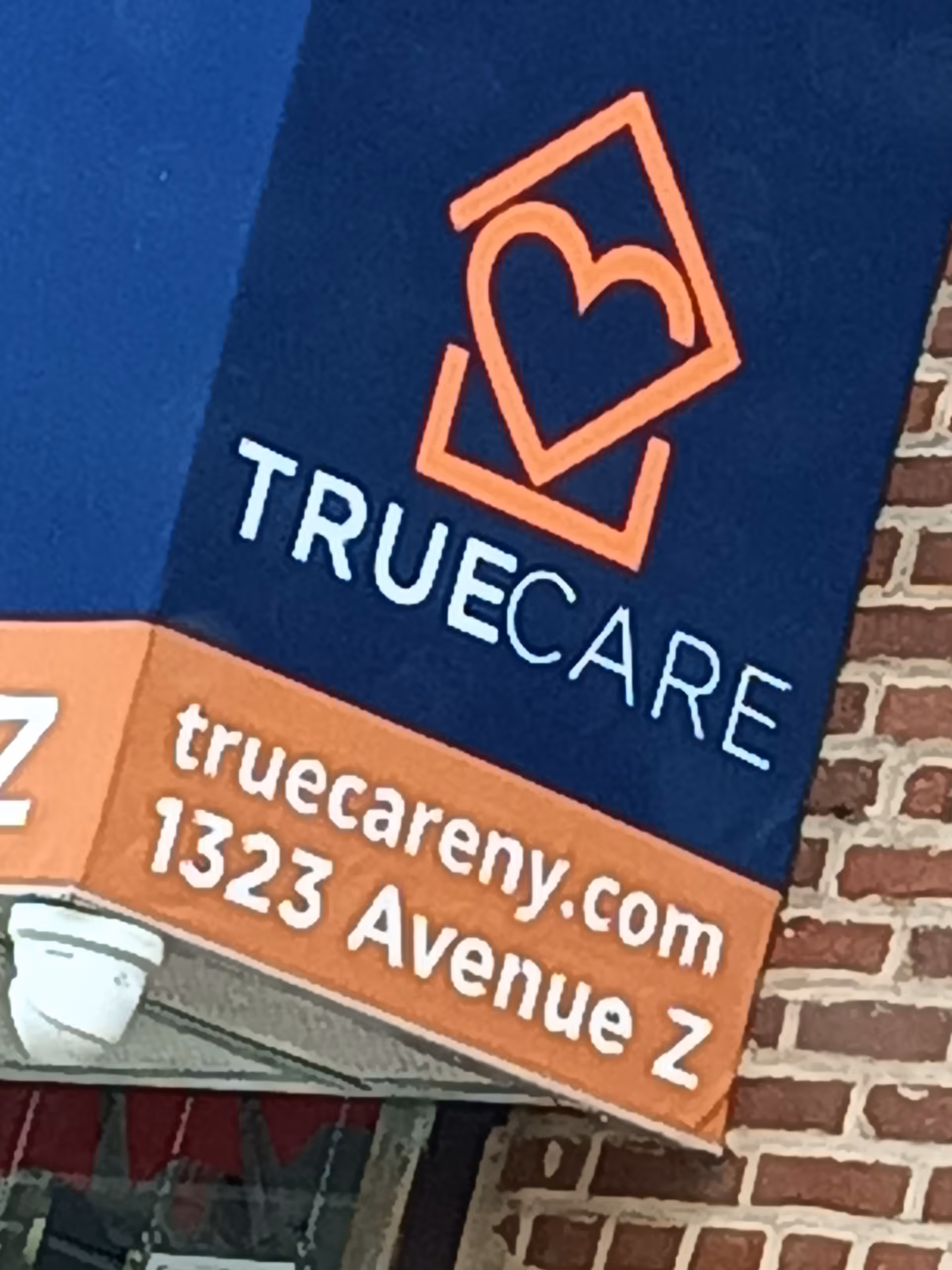 Blue TrueCare sign with orange heart logo on brick building exterior.