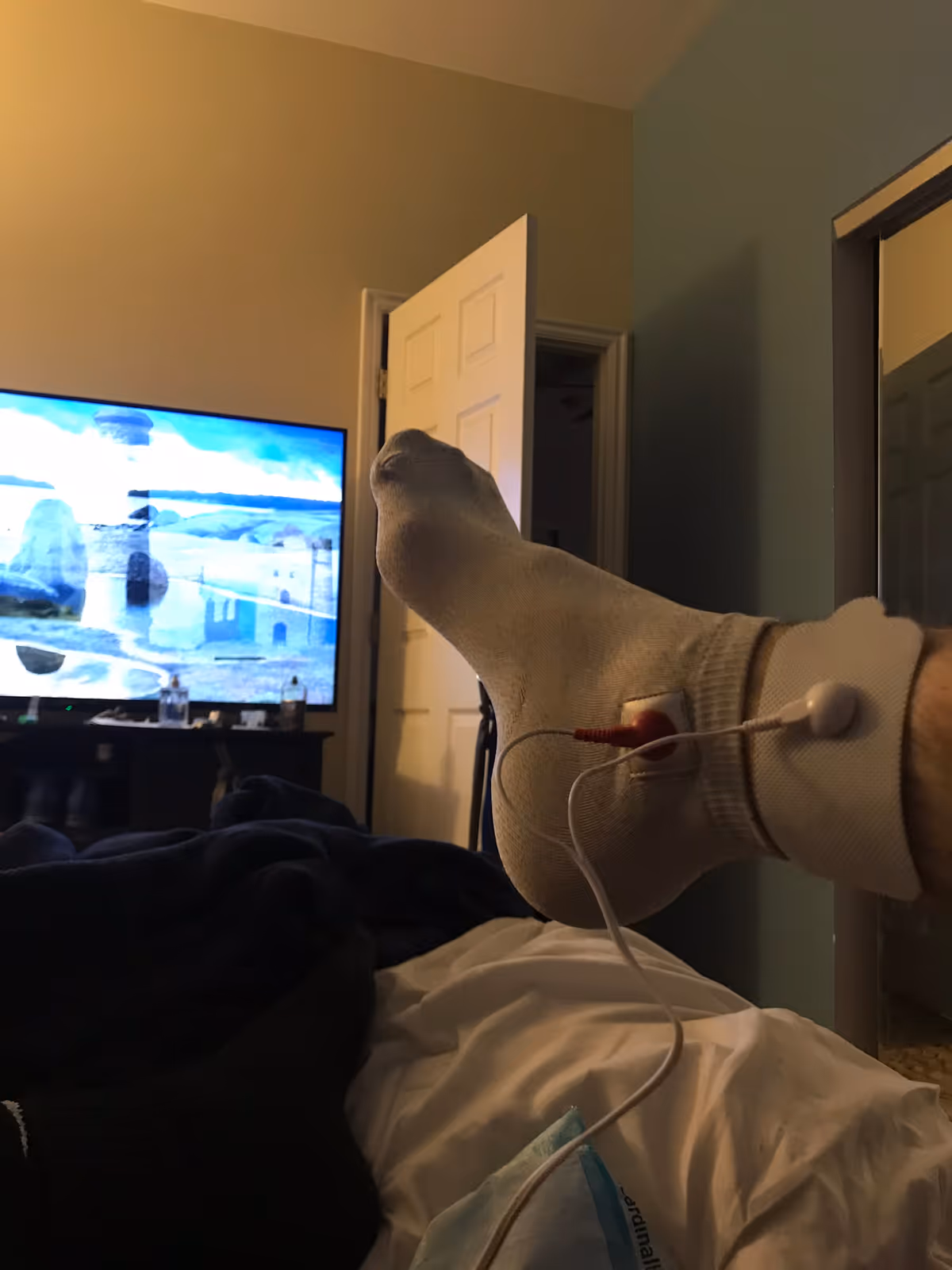 Resident's socked foot with medical sensor and wires in a dim bedroom.