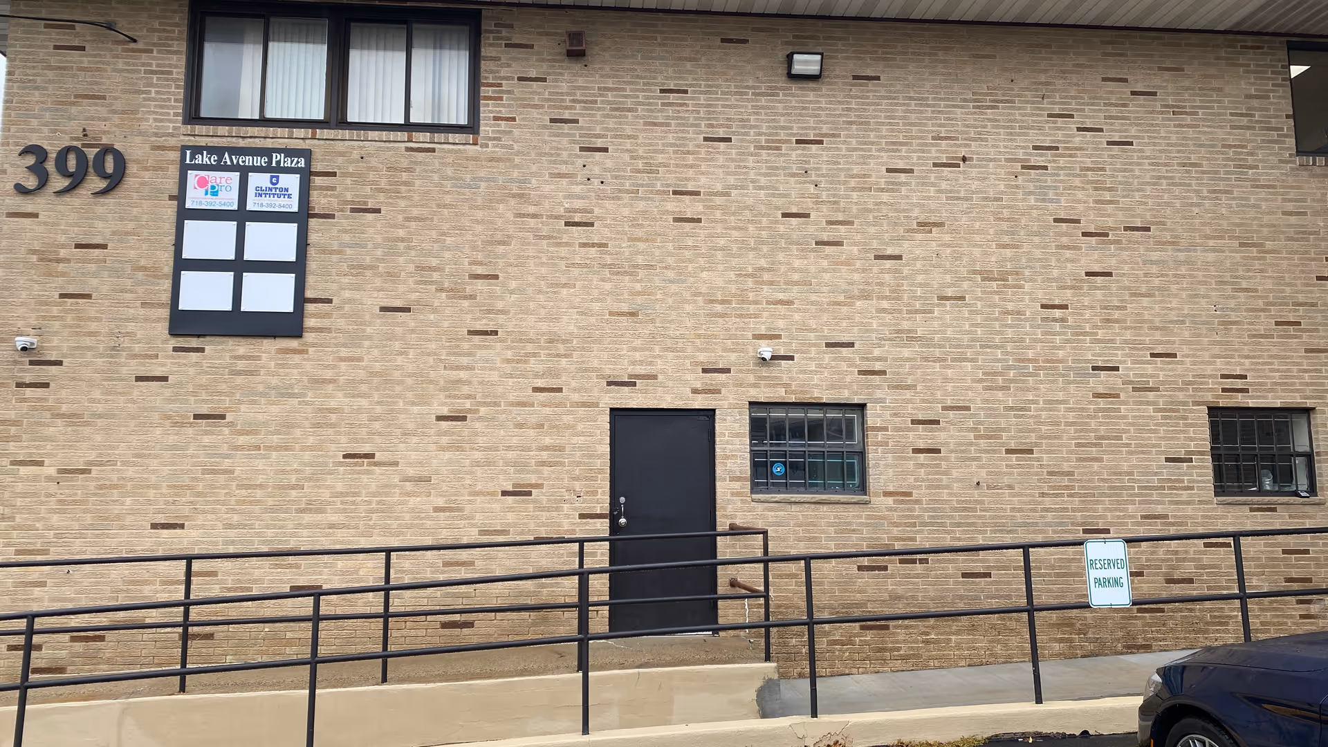 Brick building facade with a black door, windows, ramp, and parked car.