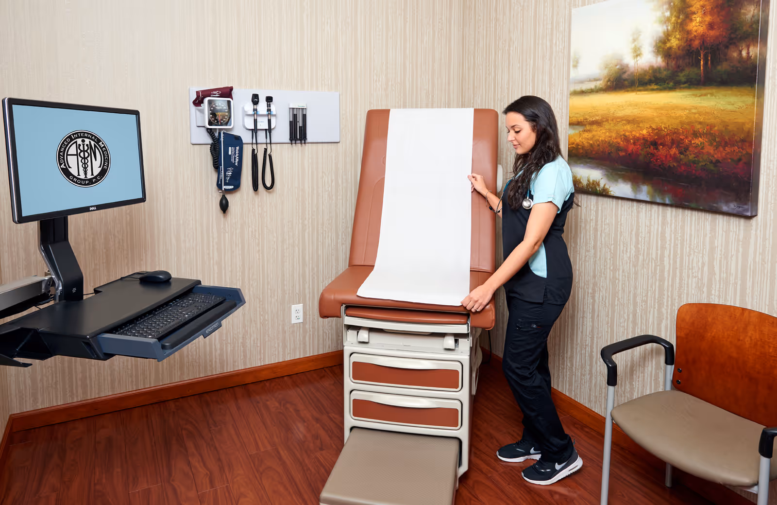Healthcare professional adjusting an exam table in a clinic room with computer monitor