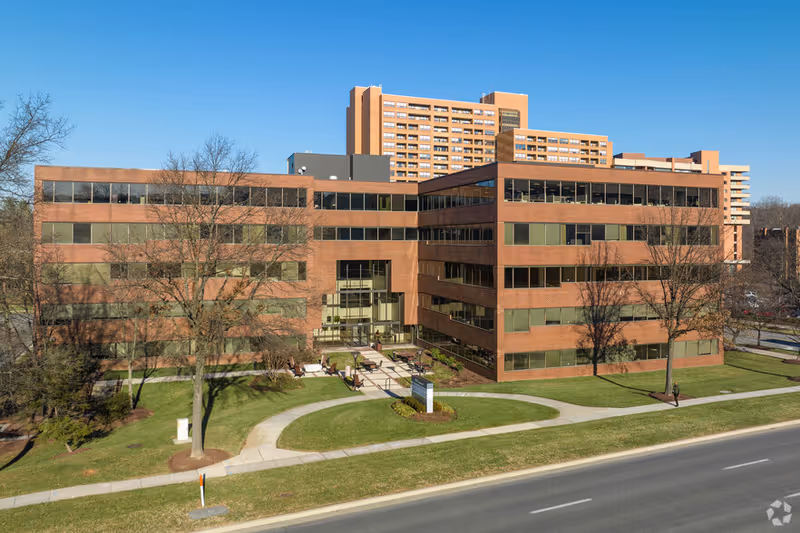 Exterior view of a large brick senior living facility with a curved walkway and green lawn.