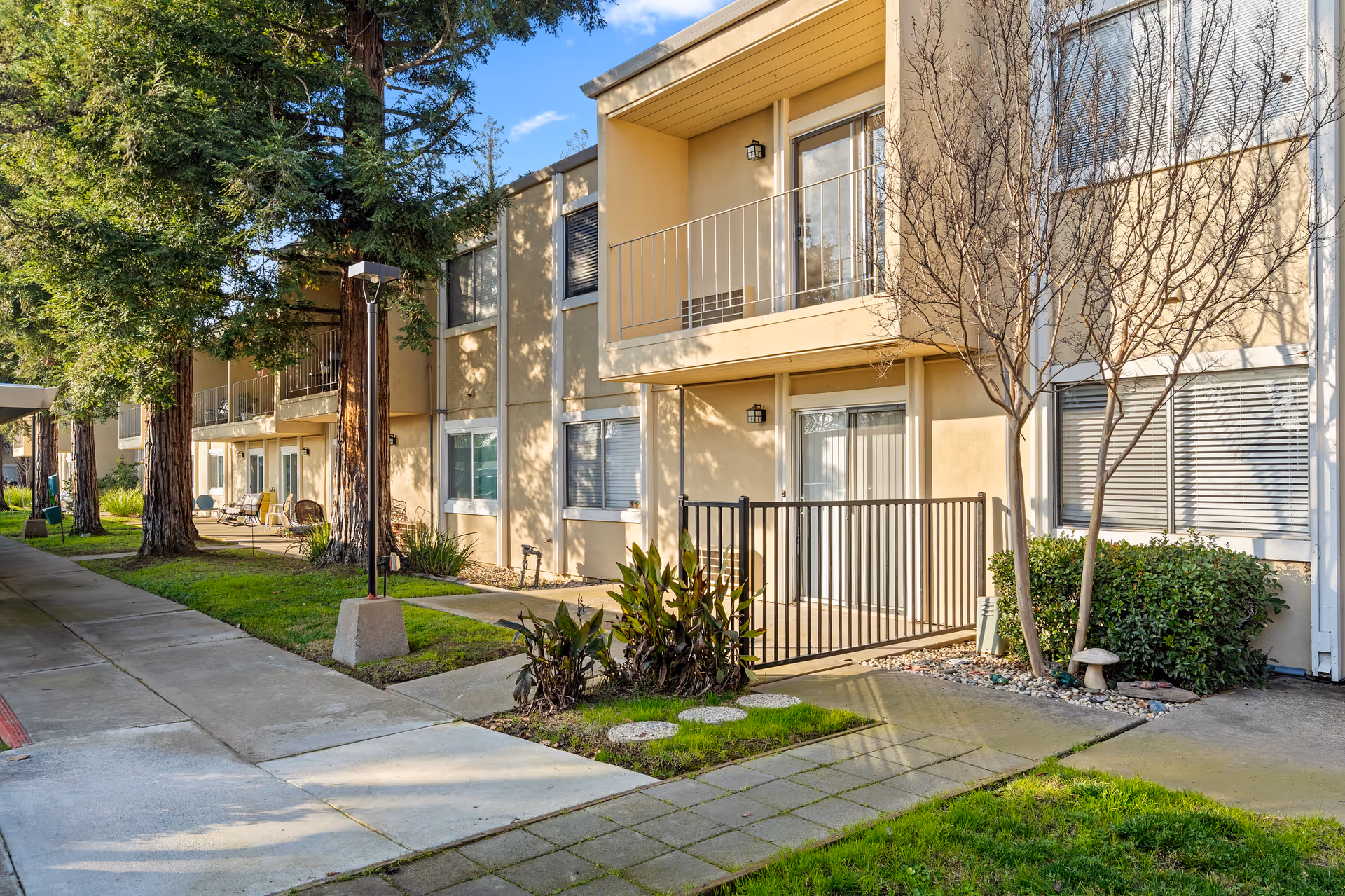 Two-story senior living building with balconies, walkway, and landscaped grounds.