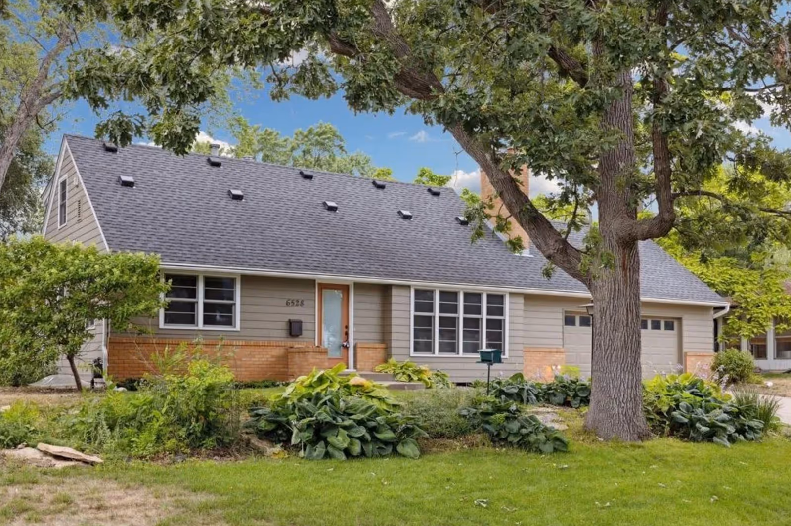 Single-story senior living residence with gray roof, beige siding, and well-kept front yard.