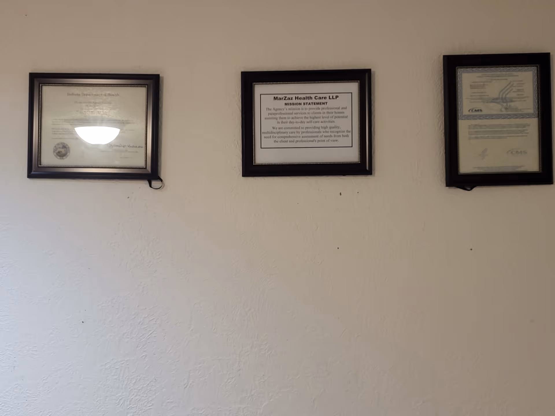 Three framed certificates hung on a textured beige wall in a hallway.