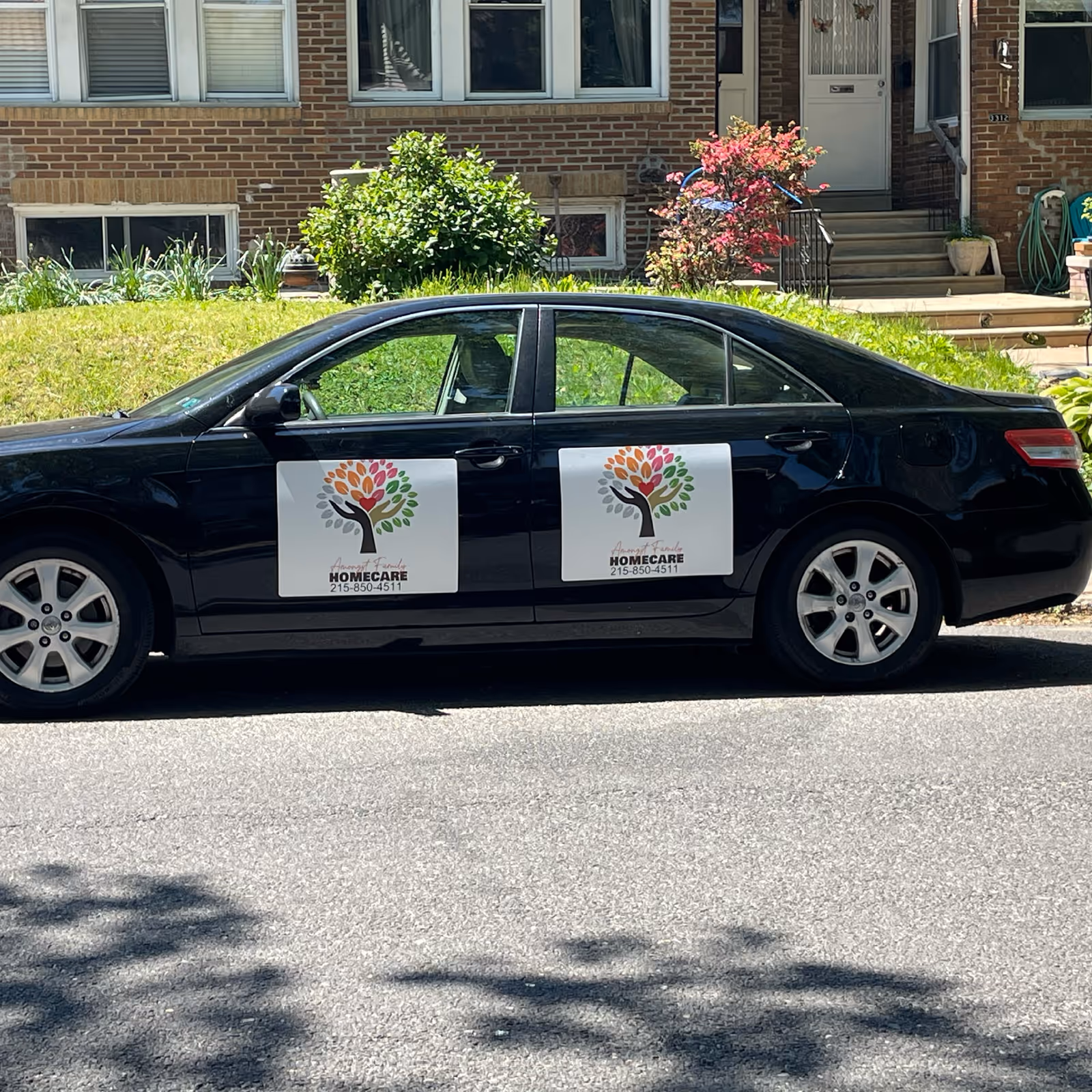 Black sedan with home care signs parked on a residential street in front of brick building.