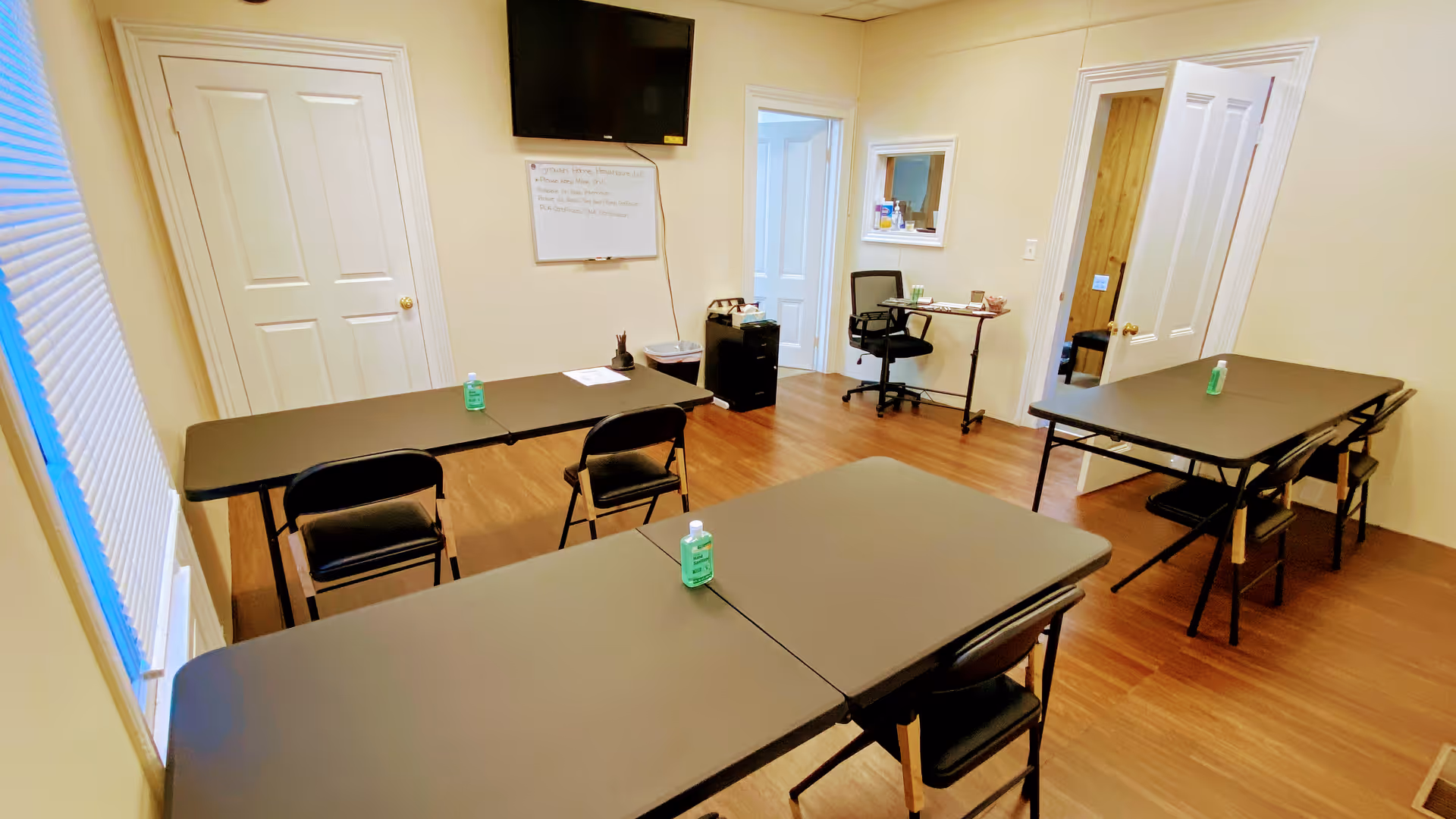 Several rectangular folding tables with chairs arranged in a meeting room; sanitizer bottles on each table.